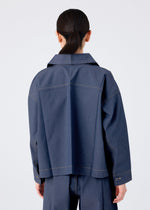 A person with long dark hair in a low ponytail is shown from the back, wearing the FLAT DENIM jacket and pants by me ISSEY MIYAKE, featuring a realistic denim texture, against a plain light background.