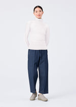 A person stands against a plain background, hands in pockets and smiling slightly, wearing me ISSEY MIYAKE FLAT DENIM loose straight pants, a white turtleneck sweater, and light gray slip-on shoes.