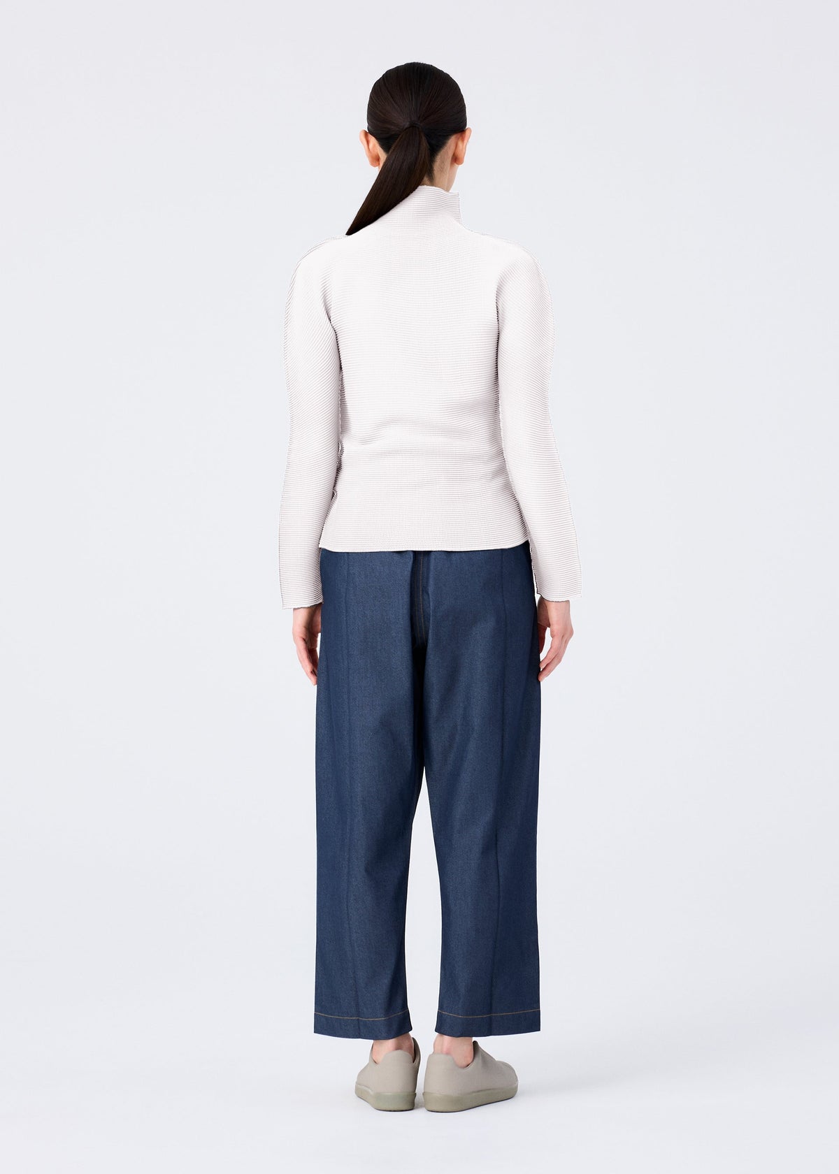 A person with long dark hair in a ponytail stands facing away, wearing a light turtleneck and FLAT DENIM straight pants by me ISSEY MIYAKE with light shoes, set against a plain white background. view 5 of 5