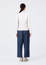 A person with long dark hair in a ponytail stands facing away, wearing a light turtleneck and FLAT DENIM straight pants by me ISSEY MIYAKE with light shoes, set against a plain white background.