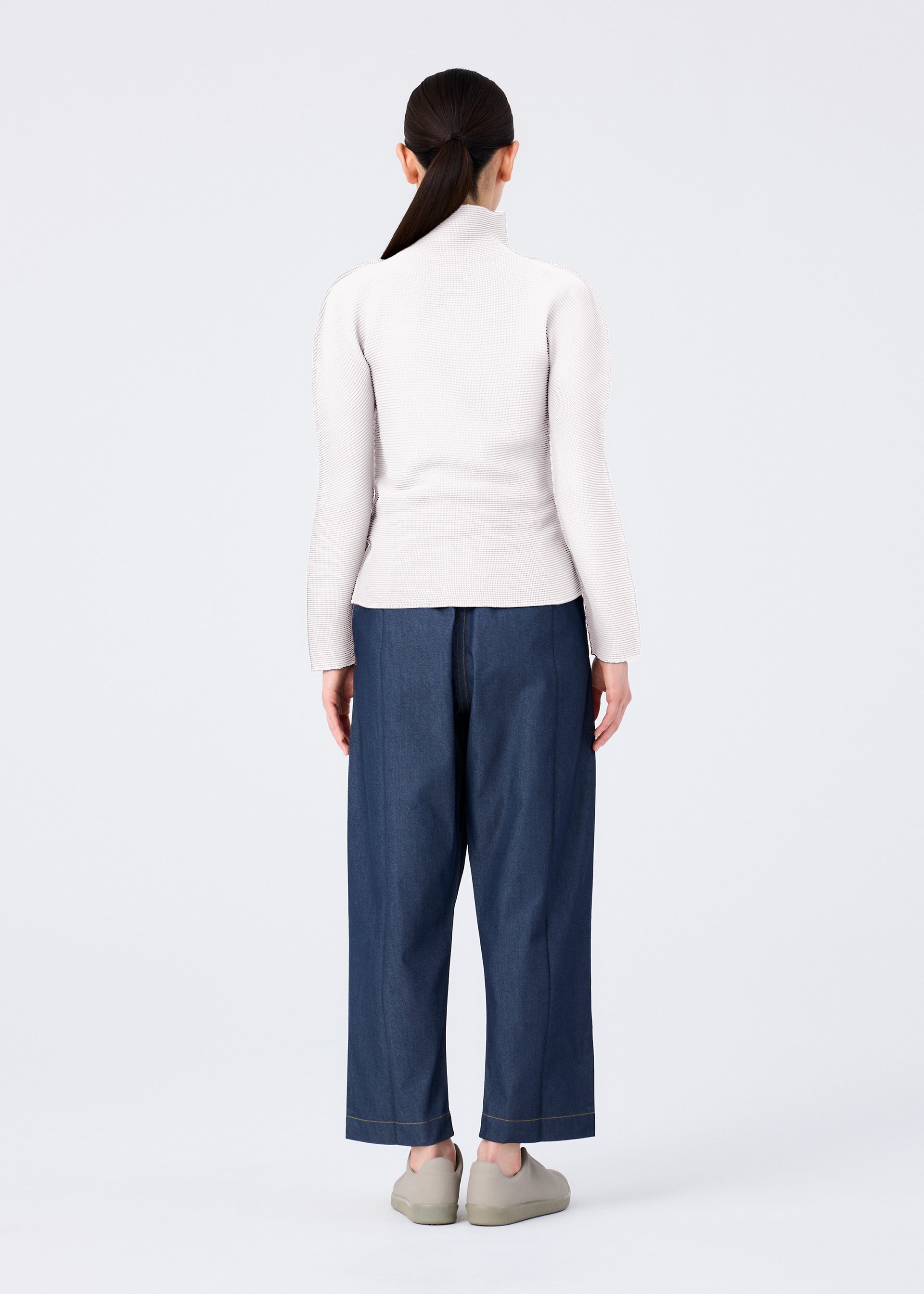 Zoomed view A person with long dark hair in a ponytail stands facing away, wearing a light turtleneck and FLAT DENIM straight pants by me ISSEY MIYAKE with light shoes, set against a plain white background.
