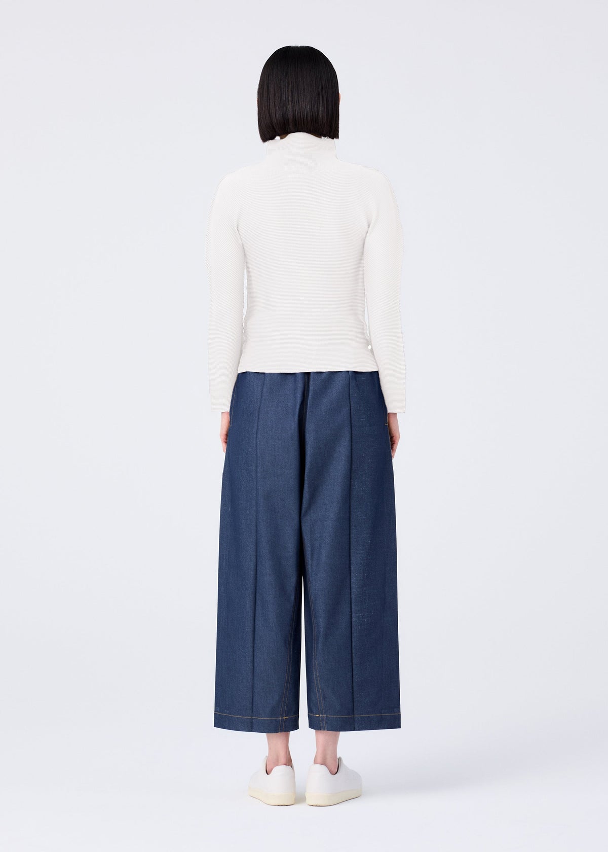 A person with straight dark hair stands facing away against a white background, wearing a white long-sleeve top, white shoes, and FLAT DENIM wide-leg pants by me ISSEY MIYAKE. view 5 of 5