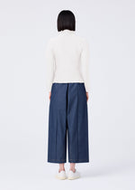 A person with straight dark hair stands facing away against a white background, wearing a white long-sleeve top, white shoes, and FLAT DENIM wide-leg pants by me ISSEY MIYAKE.