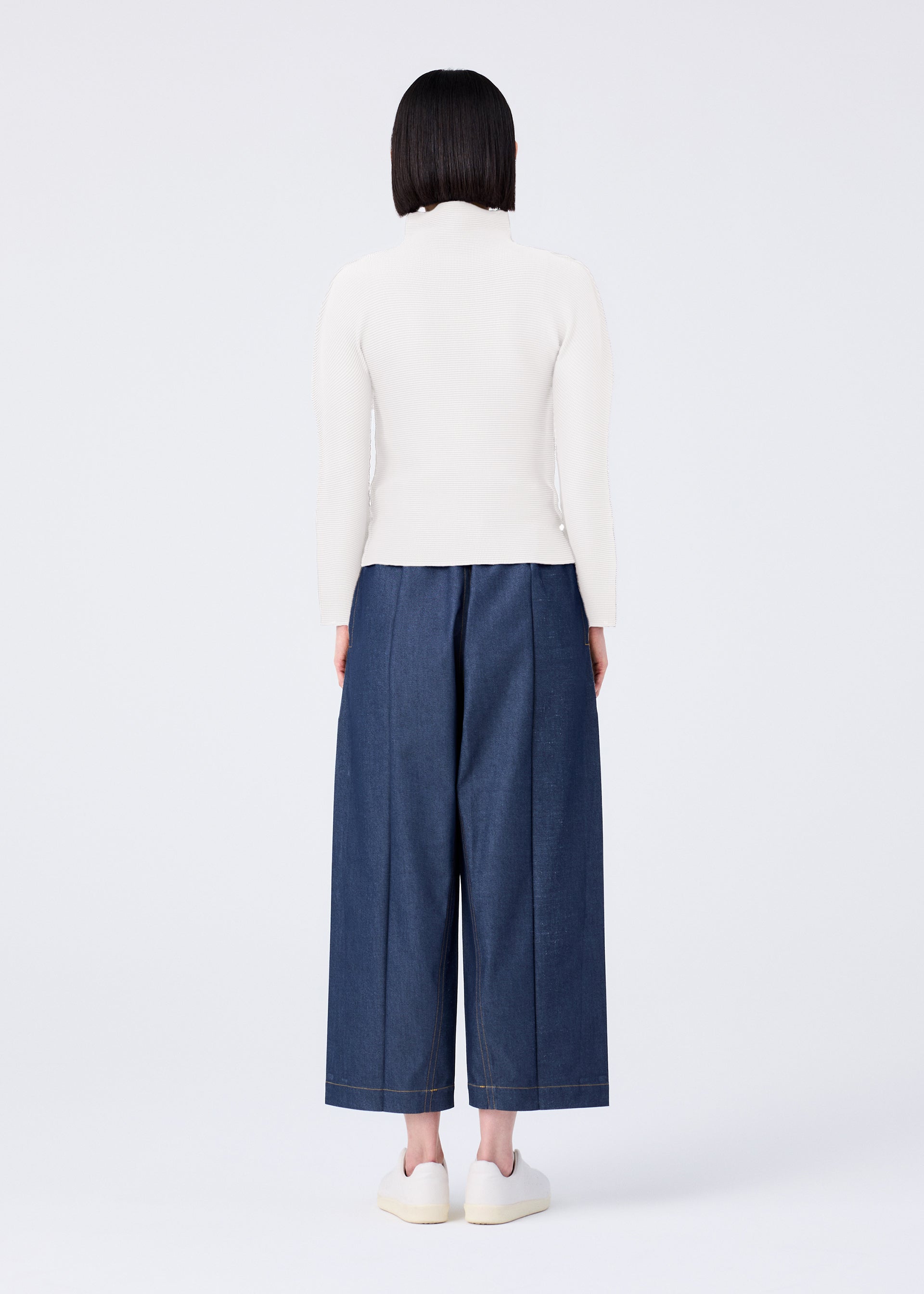 Zoomed view A person with straight dark hair stands facing away against a white background, wearing a white long-sleeve top, white shoes, and FLAT DENIM wide-leg pants by me ISSEY MIYAKE.