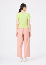 A woman faces away from the camera wearing me ISSEY MIYAKE’s FLAT DENIM SEASONAL salmon pink straight pants, a light green short-sleeve top, and white shoes, posed against a plain white background.