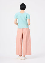 A person with short black hair stands facing away, wearing a light blue short-sleeve top, white shoes, and salmon pink FLAT DENIM SEASONAL pants by me ISSEY MIYAKE against a plain white background.