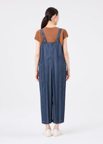 A woman stands facing away, wearing a brown short-sleeve top and the me ISSEY MIYAKE DENIM PLEATS BOTTOM—blue wide-leg salopettes with vertical stripes crafted from recycled polyester denim. Her straight dark hair is tied back, and she wears white shoes against a plain white background.