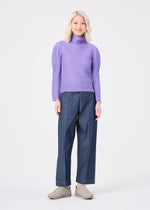 A person with light blonde hair is smiling against a plain white background while wearing the me ISSEY MIYAKE STRETCH PLEATS 3 long-sleeved lavender turtleneck, paired with wide-leg denim pants and beige shoes.