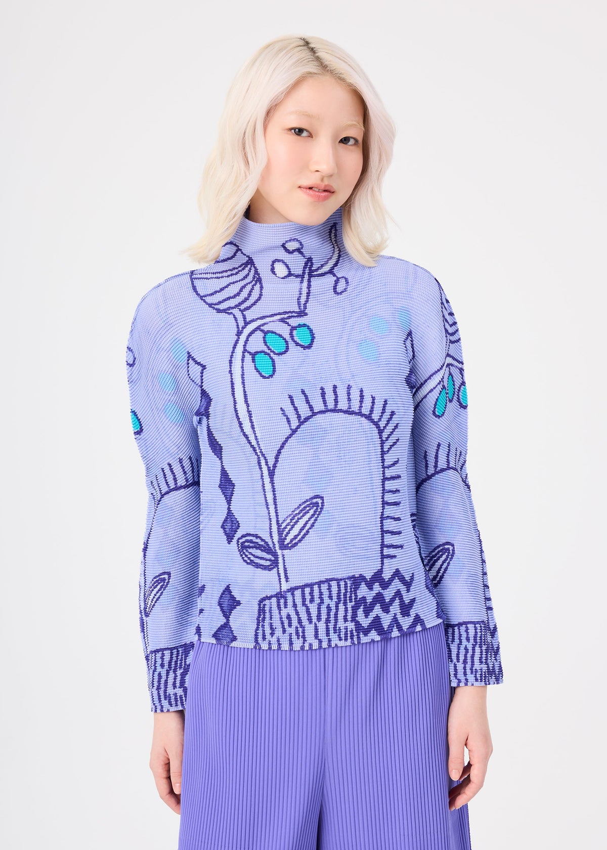 Zoomed view A person with light blonde hair wears the me ISSEY MIYAKE PLANT stretch pleats top in lavender, featuring abstract blue and teal plant patterns, paired with pleated purple pants, standing against a plain white background.