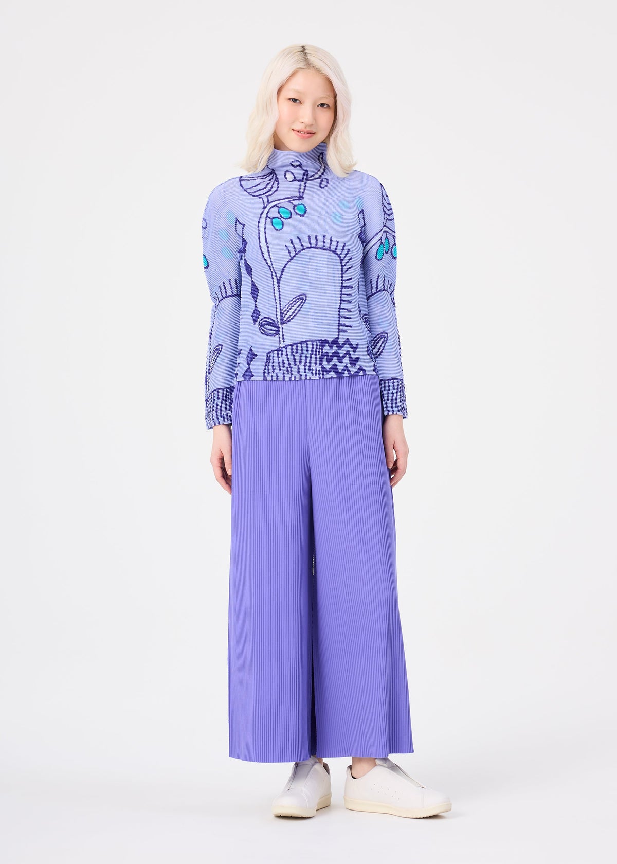 A person with light hair wears the “PLANT” high-neck long-sleeve stretch pleats top by me ISSEY MIYAKE, featuring a subtle plant pattern in light blue, paired with wide-legged pleated lavender pants and white shoes, standing against a plain white background. view 7 of 7
