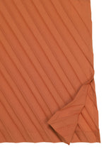 A close-up of the ANGLE PLEATS SHIRT by me ISSEY MIYAKE, highlighting its rust-colored, versatile fabric with diagonal stripes, and one corner folded to reveal the reverse side.