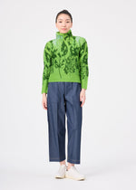A woman stands against a white background, wearing the LEAF shirt by me ISSEY MIYAKE, blue wide-leg pants, and white slip-on shoes. Her hair is pulled back as she looks directly at the camera.