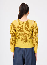 A person with a sleek ponytail faces away, wearing the LEAF yellow round-neck top with brown abstract leaf pattern by me ISSEY MIYAKE and blue high-waisted pants, set against a plain white background.