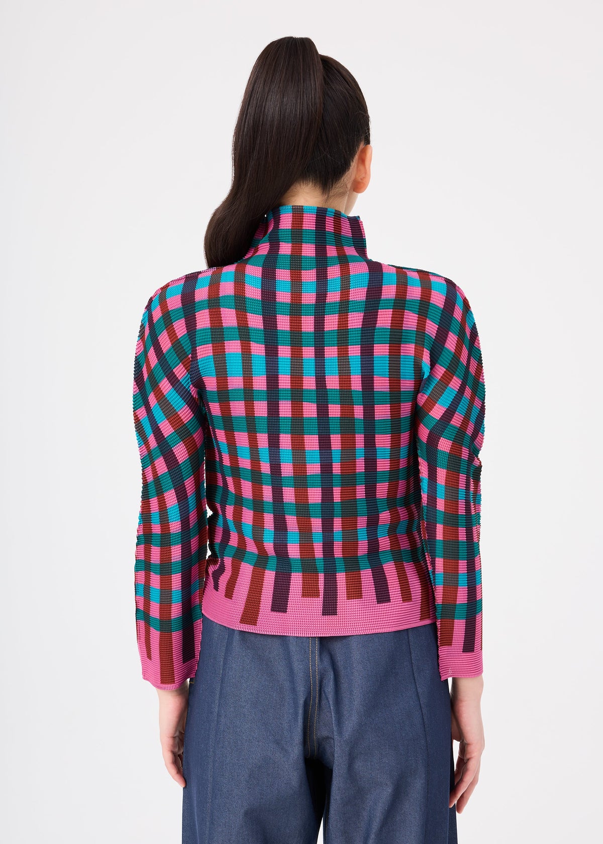 Zoomed view A person with long dark hair in a ponytail wears the TAPE CHECK top by me ISSEY MIYAKE and loose blue jeans, facing away from the camera against a white background.