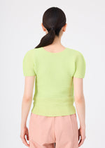 A person with long dark hair in a low ponytail is seen from behind, wearing the me ISSEY MIYAKE STRETCH PLEATS 1 light green short-sleeved top and light pink pants against a plain white background.