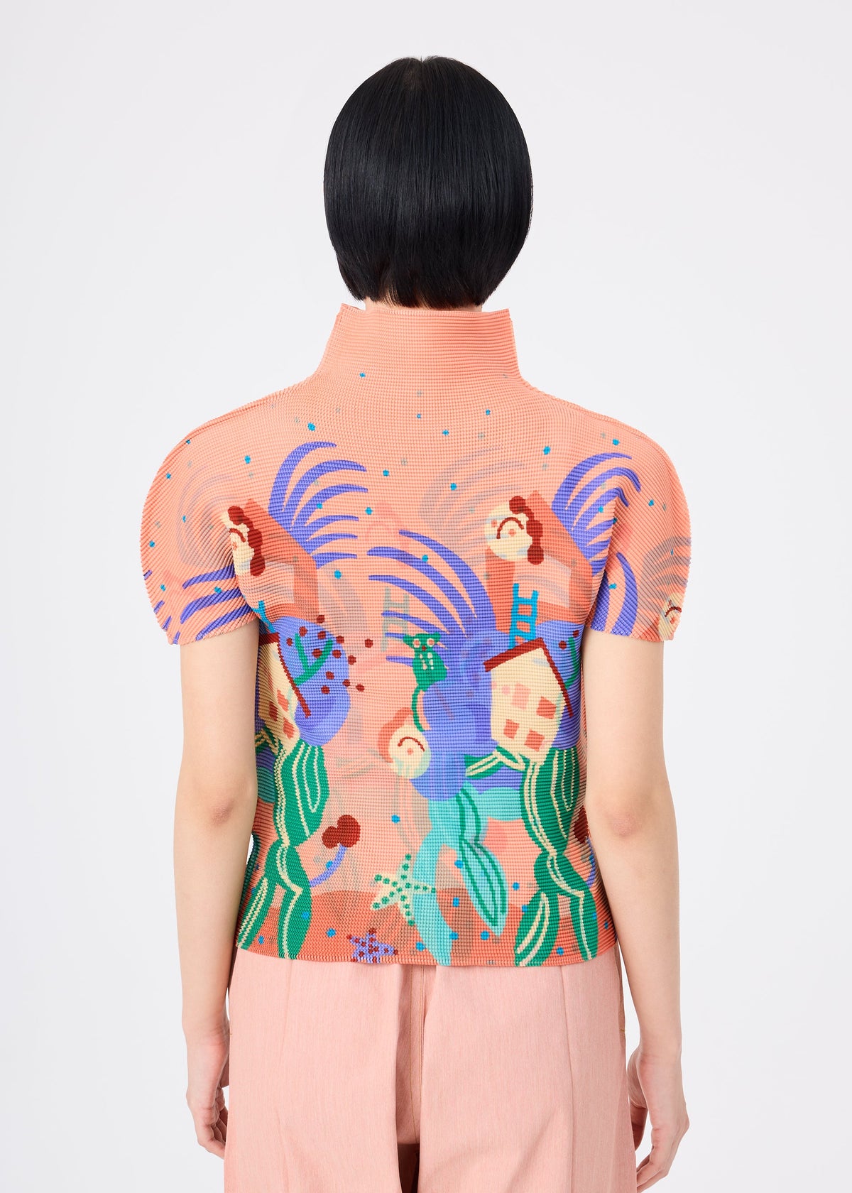 A person with short black hair is seen from behind wearing the ISLAND high-neck stretchy top by me ISSEY MIYAKE in peach, featuring bold colorful abstract patterns and a playful Philippines tarsier motif, paired with light pink pants. view 5 of 6