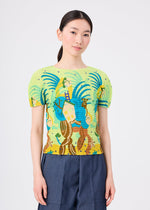 A woman with long dark hair in a low ponytail wears the ISLAND short-sleeved stretch pleats top by me ISSEY MIYAKE, featuring colorful Philippine motifs, paired with blue high-waisted pants against a plain light background.