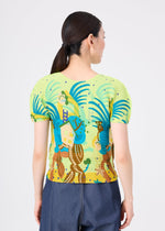 A woman with dark hair in a low ponytail is seen from the back, wearing the ISLAND stretch pleats top by me ISSEY MIYAKE, featuring abstract blue, green, and brown Philippine-inspired patterns with dark blue pants against a plain background.