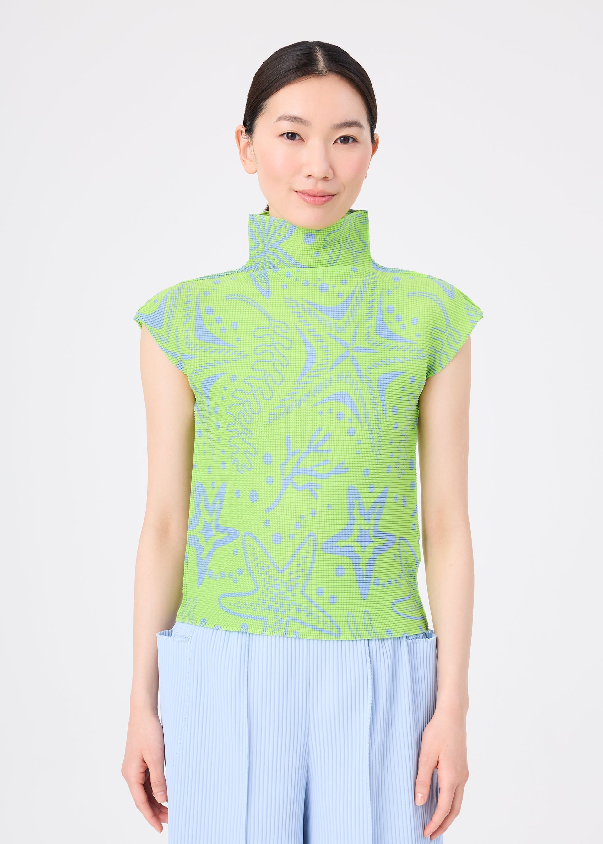 Zoomed view A woman with straight dark hair tied back wears the STARFISH high-neck top from me ISSEY MIYAKE, featuring a blue starfish pattern and stretch pleats, paired with light blue pleated pants against a plain white background.
