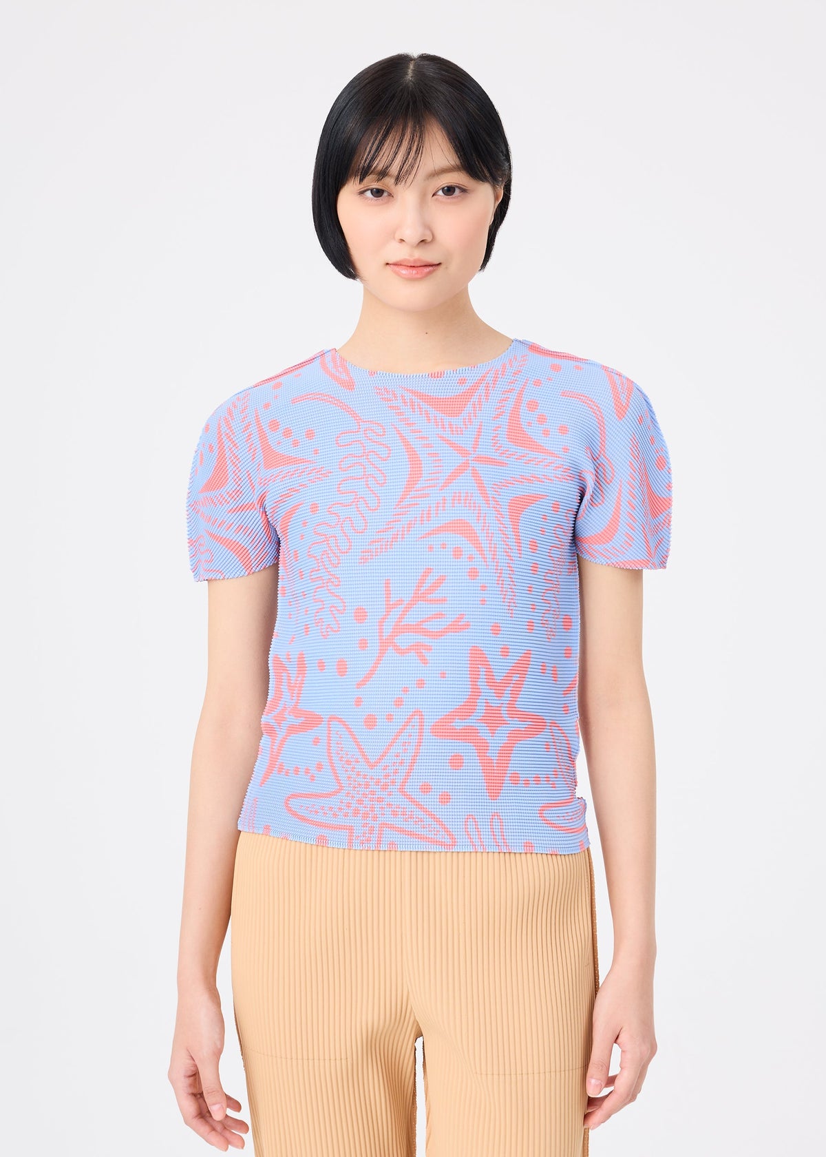 A woman with short black hair wears the me ISSEY MIYAKE STARFISH light blue knit top with a starfish and seaweed pattern, paired with beige pleated pants, standing against a plain white background. view 5 of 7