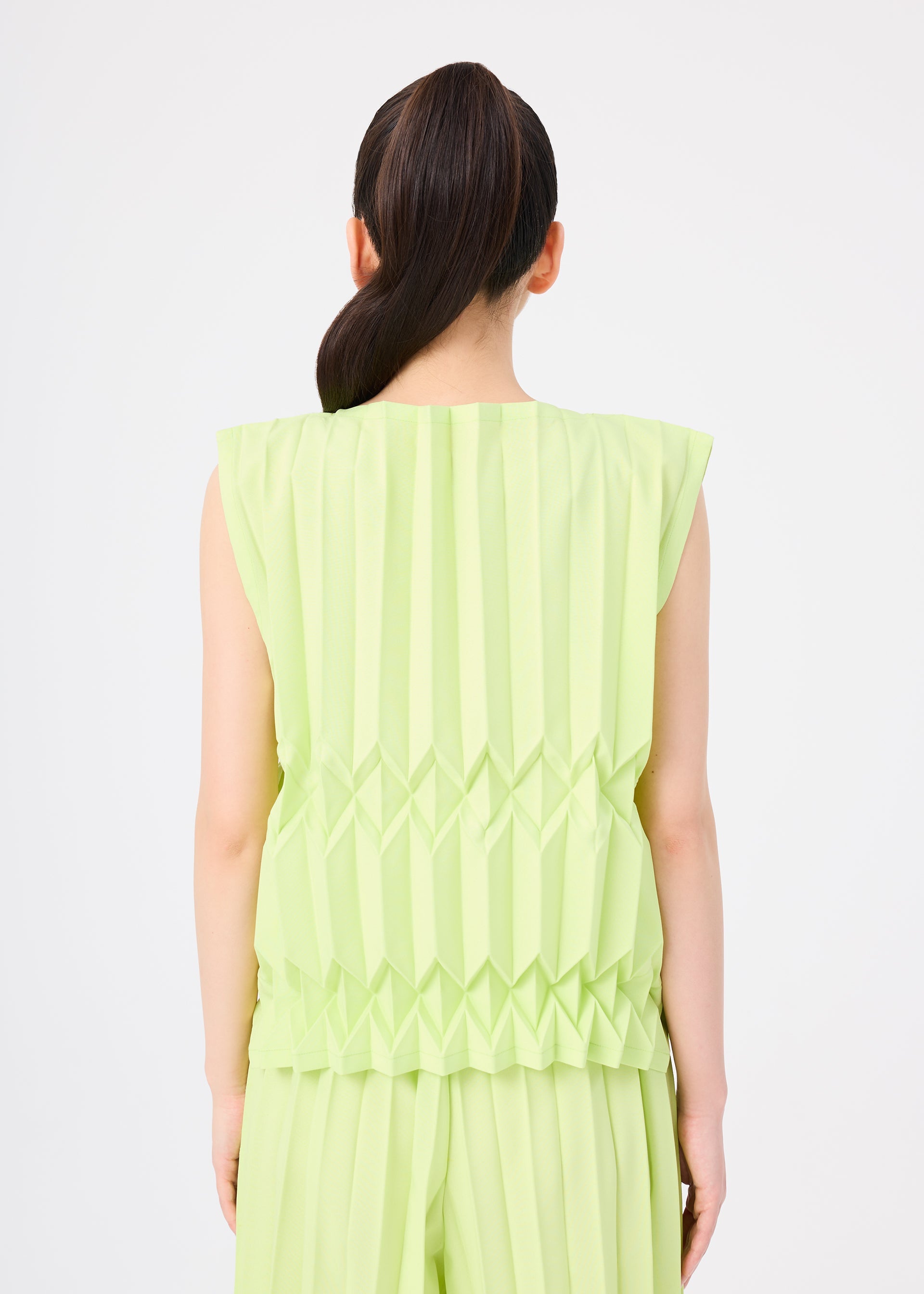 Zoomed view A person with long dark hair in a ponytail is shown from the back, wearing the TREE PLEATS sleeveless top and matching pants by me ISSEY MIYAKE, featuring hand-pleated three-dimensional patterns against a plain white background.