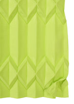 A close-up of TREE PLEATS by me ISSEY MIYAKE shows bright green fabric with hand pleating, forming a geometric 3D diamond pattern and a slightly wrinkled bottom corner.