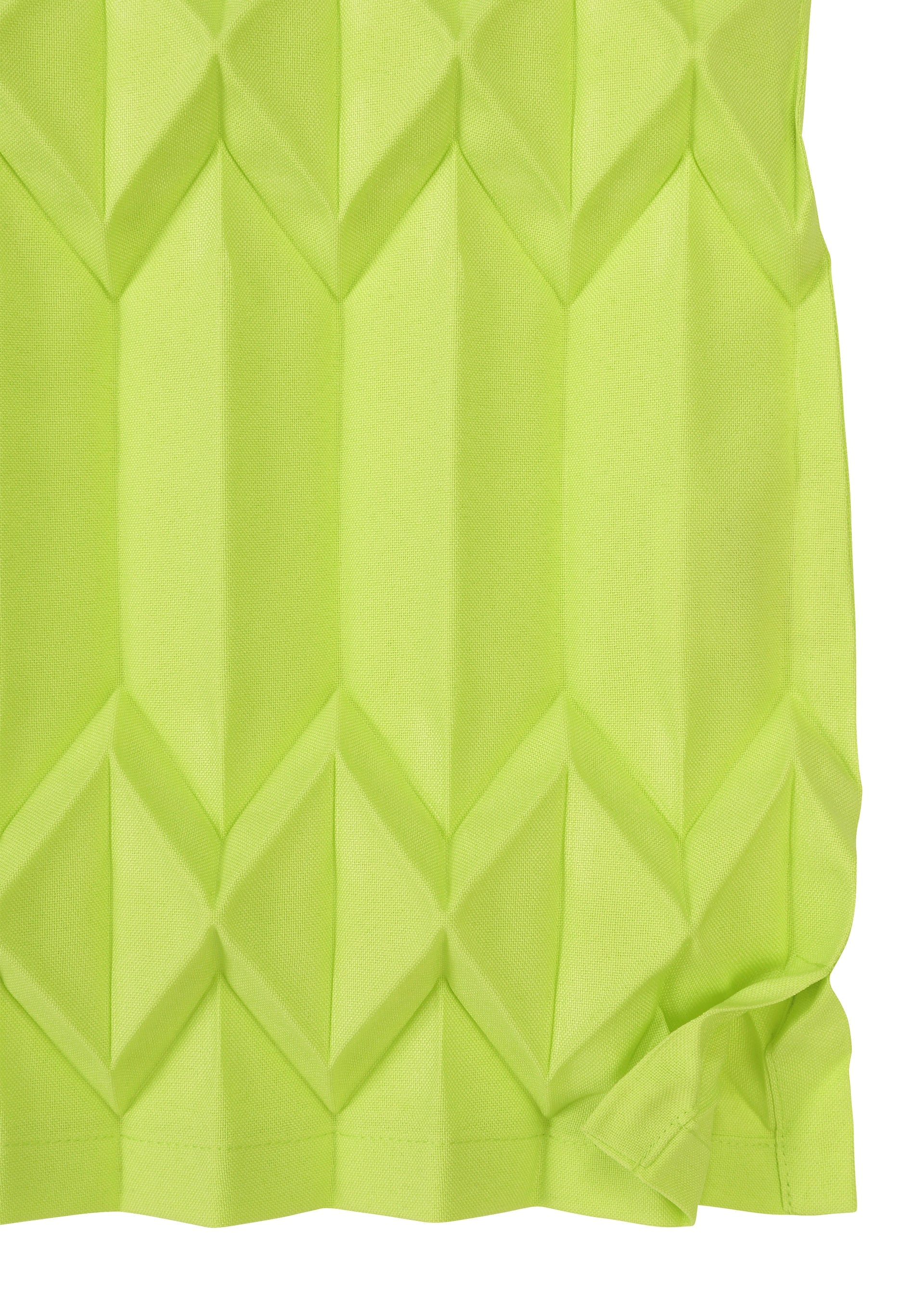 Zoomed view A close-up of TREE PLEATS by me ISSEY MIYAKE shows bright green fabric with hand pleating, forming a geometric 3D diamond pattern and a slightly wrinkled bottom corner.