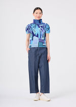 A person stands smiling against a plain white background, wearing the BUILDING blue patterned high-neck top with stretch pleats and wide-leg blue pants from me ISSEY MIYAKE, paired with white shoes.