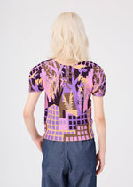A person with wavy platinum blonde hair, seen from behind, is wearing the BUILDING short-sleeved pleated round-neck top by me ISSEY MIYAKE, which features a purple, pink, and brown abstract pattern, paired with blue high-waisted pants. The background is plain and light-colored.