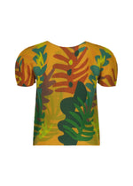 The JUNGLE top by me ISSEY MIYAKE is a pleated, short sleeve shirt with a yellow base, showcasing bold abstract green, orange, and brown leaf patterns for a stylish jungle print look. It features a round neckline and a loose fit.