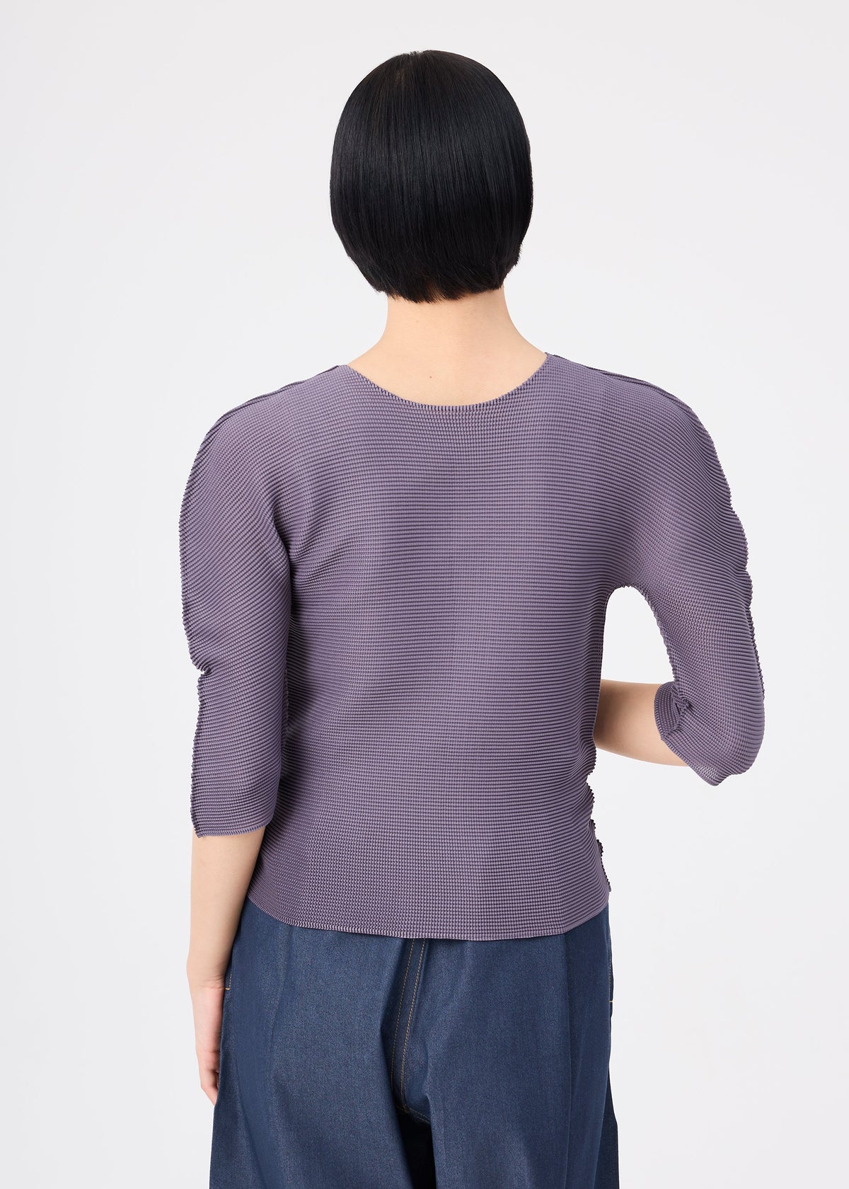 A person with short black hair wears the me ISSEY MIYAKE STRETCH PLEATS 4, a round-neck, ribbed lavender top with wide-leg dark blue pants, shown from behind against a white background. view 6 of 7