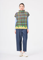 A person stands facing forward, wearing the TAPE CHECK top by me ISSEY MIYAKE over a light blue long-sleeve shirt, with loose dark blue pants and white shoes, against a plain white background.