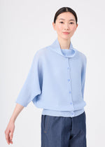 A woman with straight dark hair wears the me ISSEY MIYAKE DOLMAN STRETCH PLEATS 1, a light blue textured button-up with three-quarter sleeves, paired with dark blue jeans against a plain white background.