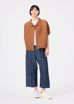 A person stands against a white background wearing the me ISSEY MIYAKE SQUARE STRETCH PLEATS relaxed fit brown short-sleeve jacket over a white shirt, paired with wide-leg blue denim pants and white slip-on shoes.