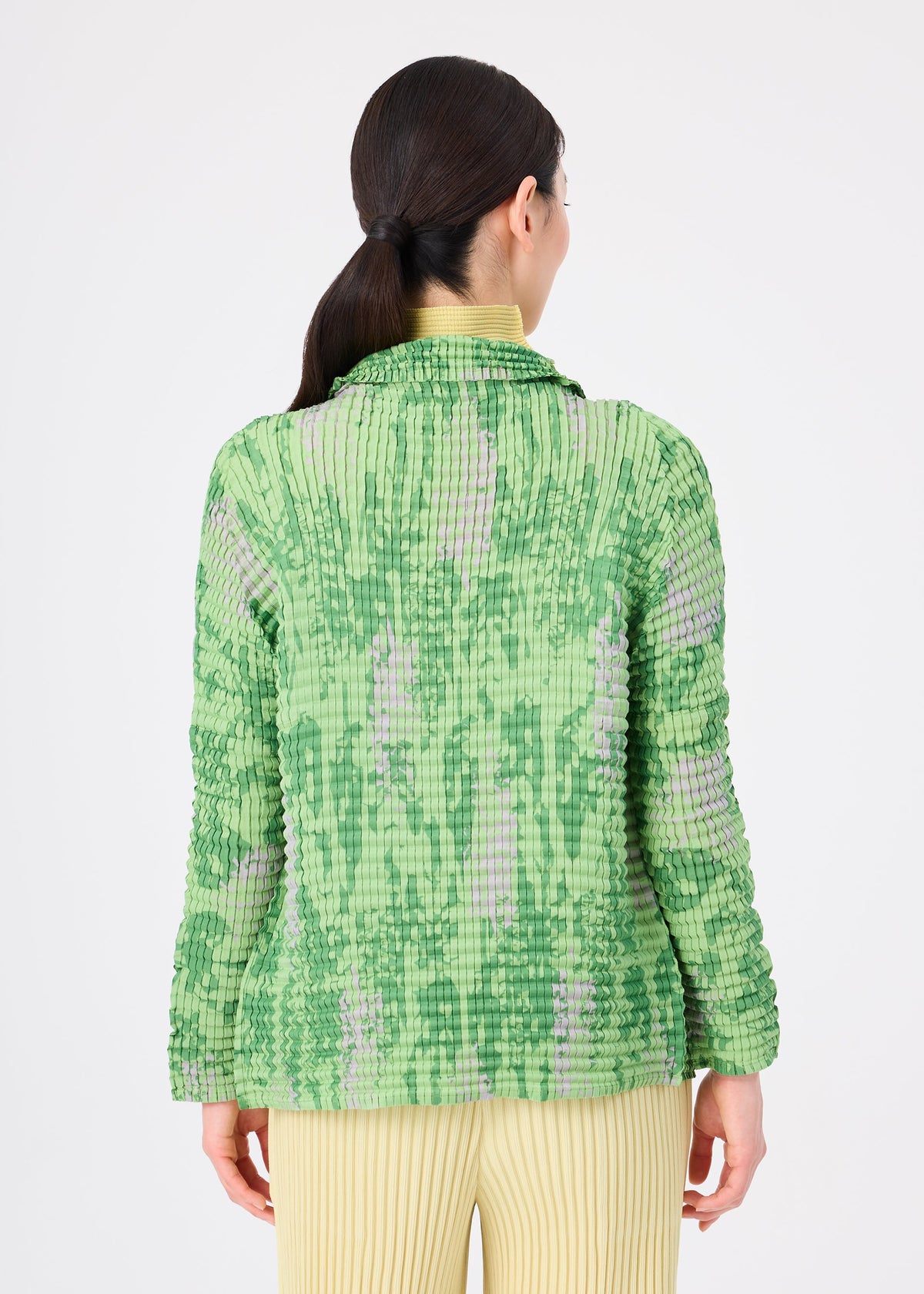A person with long, dark hair in a low ponytail wears the LEAF PLEATS SHIRT by me ISSEY MIYAKE in green and purple, paired with yellow pleated pants, standing against a plain white background, facing away. view 6 of 7