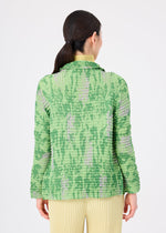 A person with long, dark hair in a low ponytail wears the LEAF PLEATS SHIRT by me ISSEY MIYAKE in green and purple, paired with yellow pleated pants, standing against a plain white background, facing away.