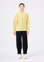 A person stands against a white background wearing the me ISSEY MIYAKE CORDUROY PLEATS yellow, ribbed button-up sweater, black wide pants, and white shoes, with straight dark hair pulled back and arms relaxed.