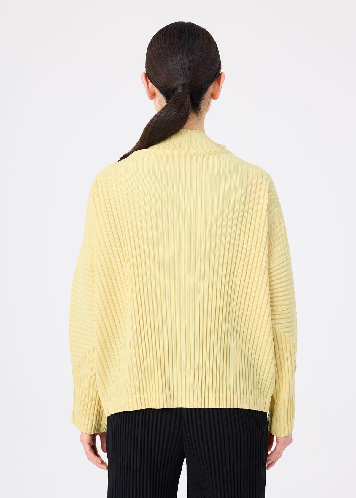 A person with long dark hair in a low ponytail models the CORDUROY PLEATS by me ISSEY MIYAKE, wearing a loose yellow pleated top and black pleated pants, seen from behind against a white background. view 7 of 8