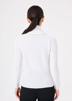 A woman is seen from behind, wearing the me ISSEY MIYAKE KNIT STRETCH PLEATS ribbed white long-sleeved cowl neck sweater with black pants. Her dark hair is styled in a sleek, low ponytail, set against a plain white background.