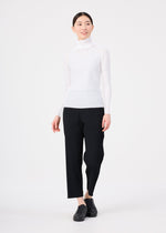A person wearing the me ISSEY MIYAKE KNIT STRETCH PLEATS, styled with black ankle-length pants and black shoes, stands against a plain white background, looking slightly to the side and smiling.