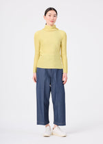 A person stands facing forward, wearing the KNIT STRETCH PLEATS 1 top by me ISSEY MIYAKE with blue wide-leg pants and white shoes, against a plain white background.