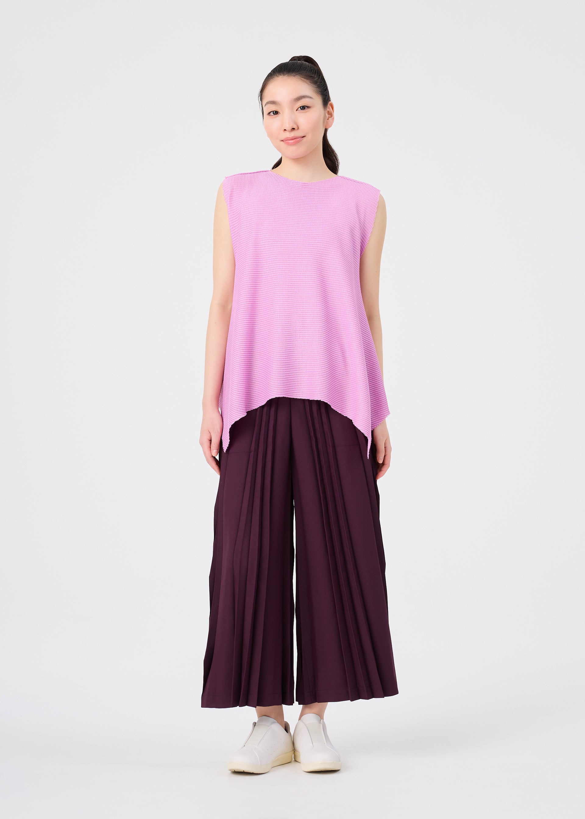 Zoomed view A woman stands facing forward against a plain white background, wearing a sleeveless, soft-textured knit top in light purple and wide, dark purple TOWER KNIT STRETCH PLEATS pants by me ISSEY MIYAKE with knit stretch pleats, paired with white slip-on shoes.