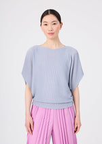 A person with straight dark hair stands facing forward against a plain white background with a neutral expression, wearing a soft-textured, light blue short-sleeved knit top and pink TOWER KNIT STRETCH PLEATS pants by me ISSEY MIYAKE.