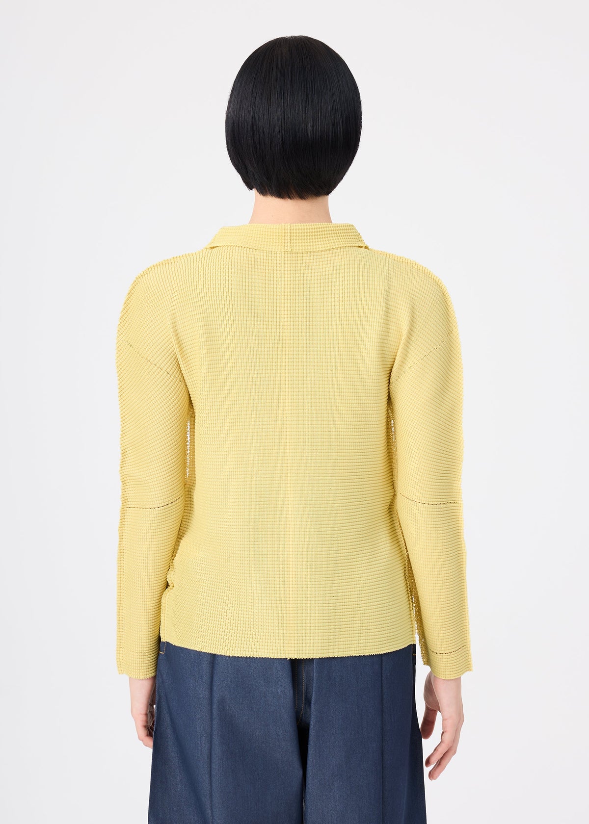 Zoomed view Person with short black hair wearing the me ISSEY MIYAKE KNIT STRETCH PLEATS 1 in yellow and dark blue pants, standing with their back to the camera against a plain white background.