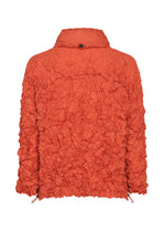 Back view of the MERINGUE PARKA by me ISSEY MIYAKE—an orange lightweight, water-repellent jacket featuring a textured, crinkled, and ruffled finish, high collar, and drawstring hem—ideal for unpredictable weather.