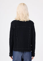A person with shoulder-length, wavy blonde hair is seen from the back wearing the me ISSEY MIYAKE CAULIFLOWER COLOR 1 black textured jacket, styled with blue pants against a plain white background.
