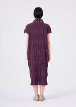 A person with short black hair stands facing away, wearing the SHRINK STRIPE knee-length dress by me ISSEY MIYAKE—a textured, purple collared dress with short sleeves and a high collar—crafted from a soft cotton-blend fabric. The look is completed with light-colored shoes and set against a plain white background.
