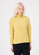 A person with light blonde hair wears the me ISSEY MIYAKE ROUND CAULIFLOWER yellow textured turtleneck top and black pants, smiling gently at the camera against a plain white background.