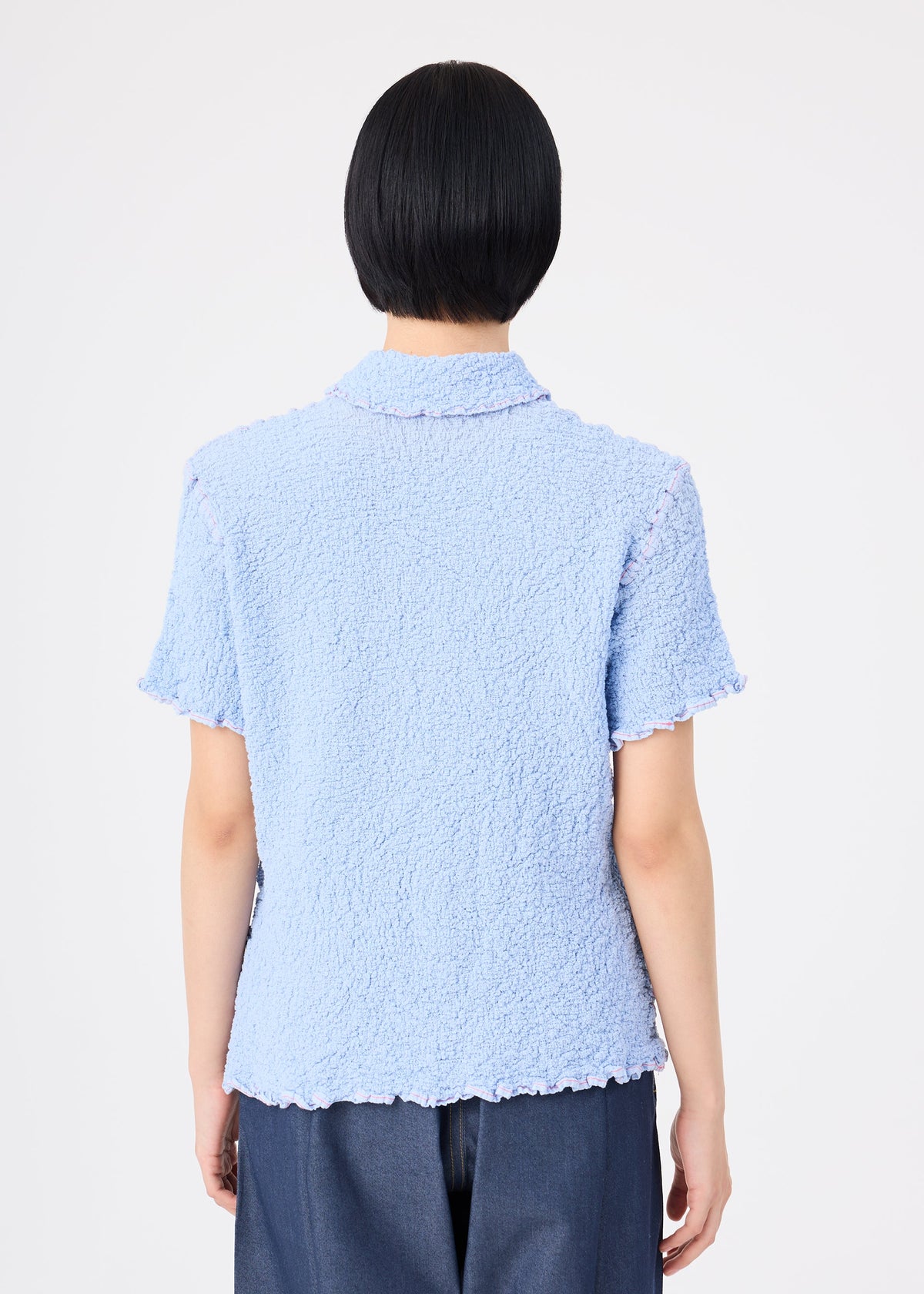 A person with short black hair is seen from behind, wearing the CAULIFLOWER COLOR 1 top by me ISSEY MIYAKE and dark pants, standing against a plain white background. view 6 of 7