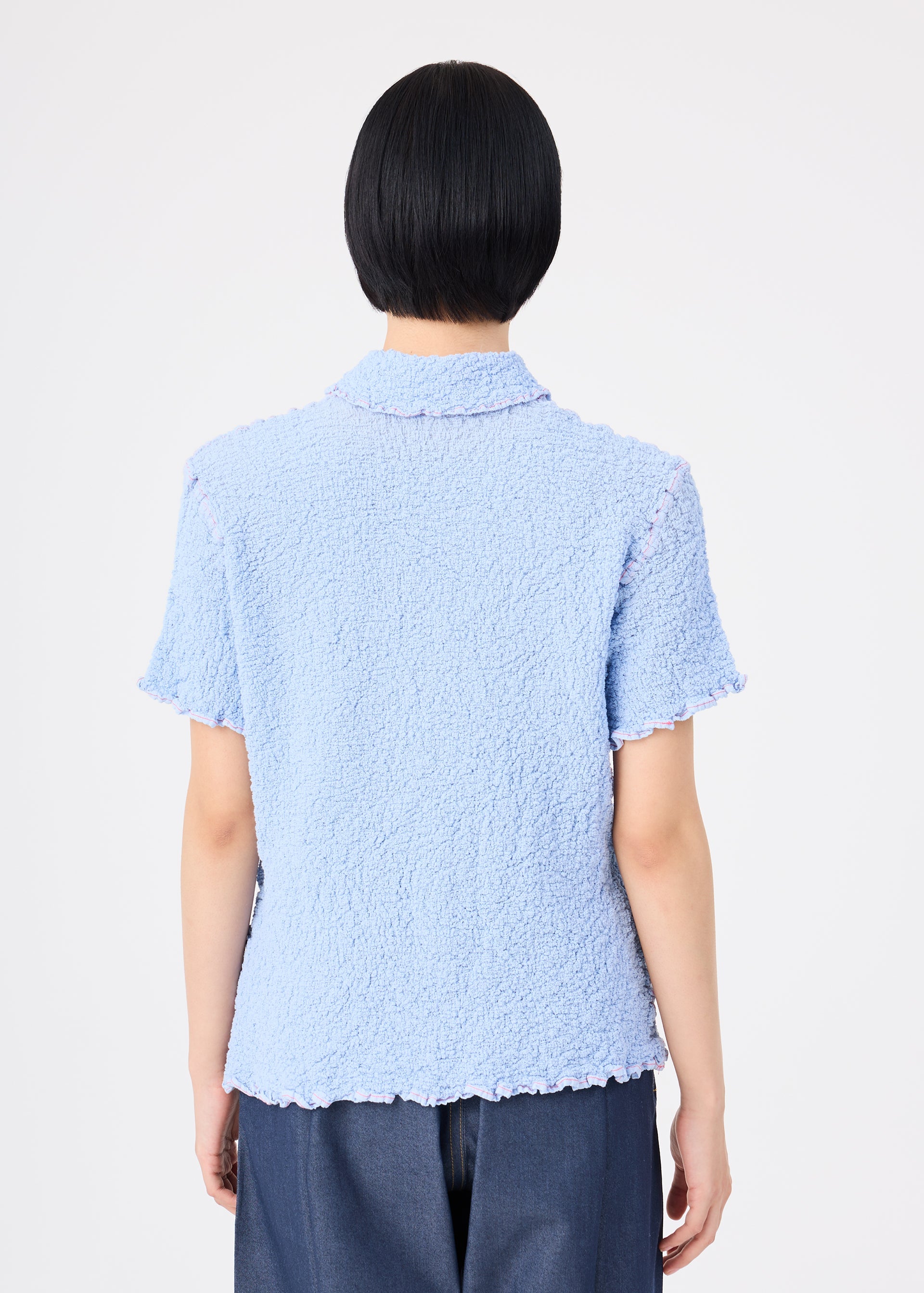 Zoomed view A person with short black hair is seen from behind, wearing the CAULIFLOWER COLOR 1 top by me ISSEY MIYAKE and dark pants, standing against a plain white background.